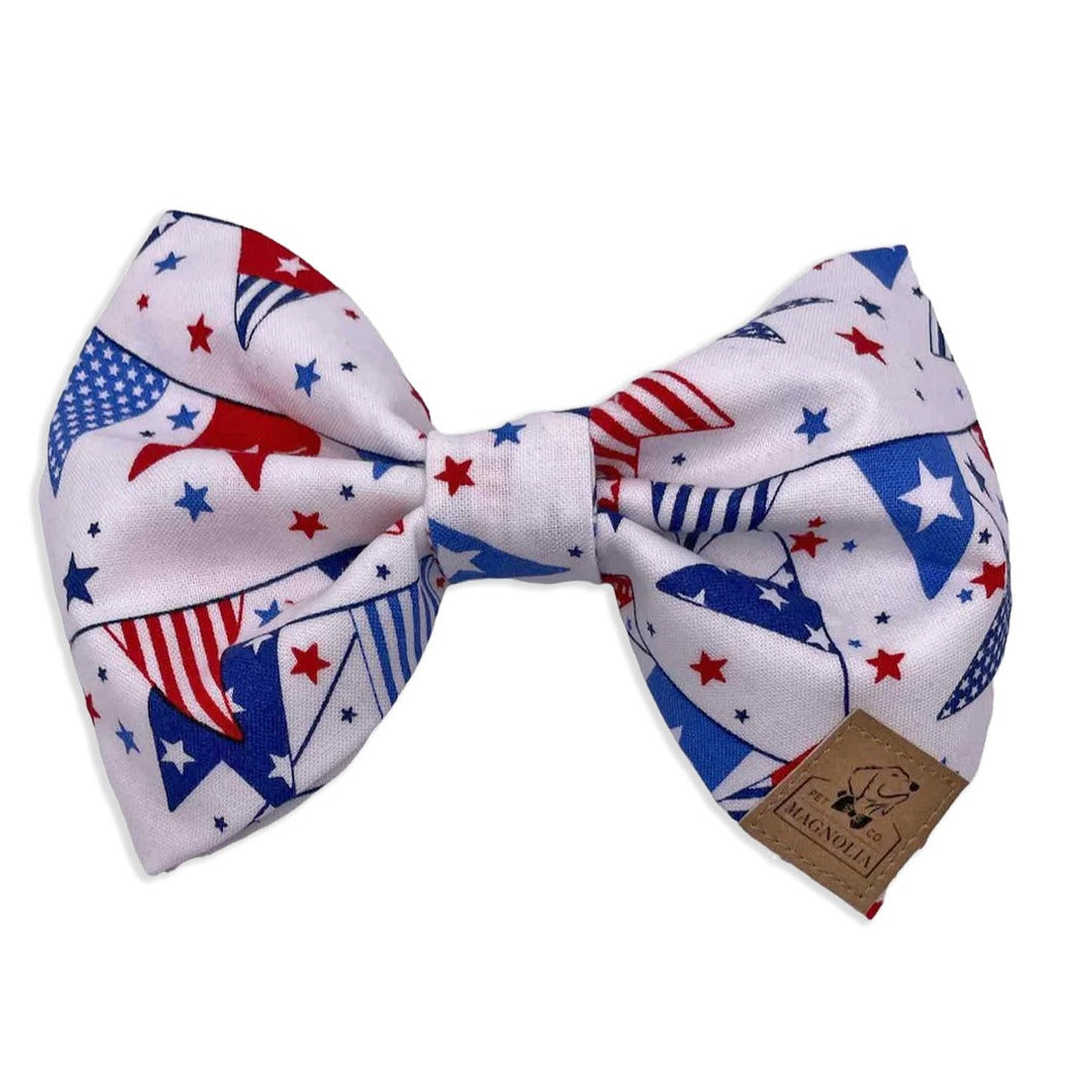 Dog bow tie featuring a lively pattern of red, white, and blue pennants against a crisp white fabric background by Magnolia Pet Company.