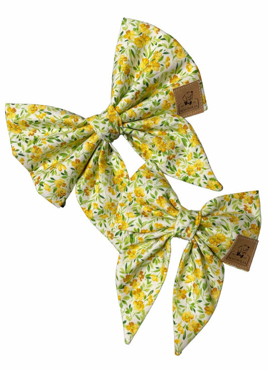 This delightful bow is crafted from crisp white fabric, beautifully adorned with vibrant yellow and green floral pattern